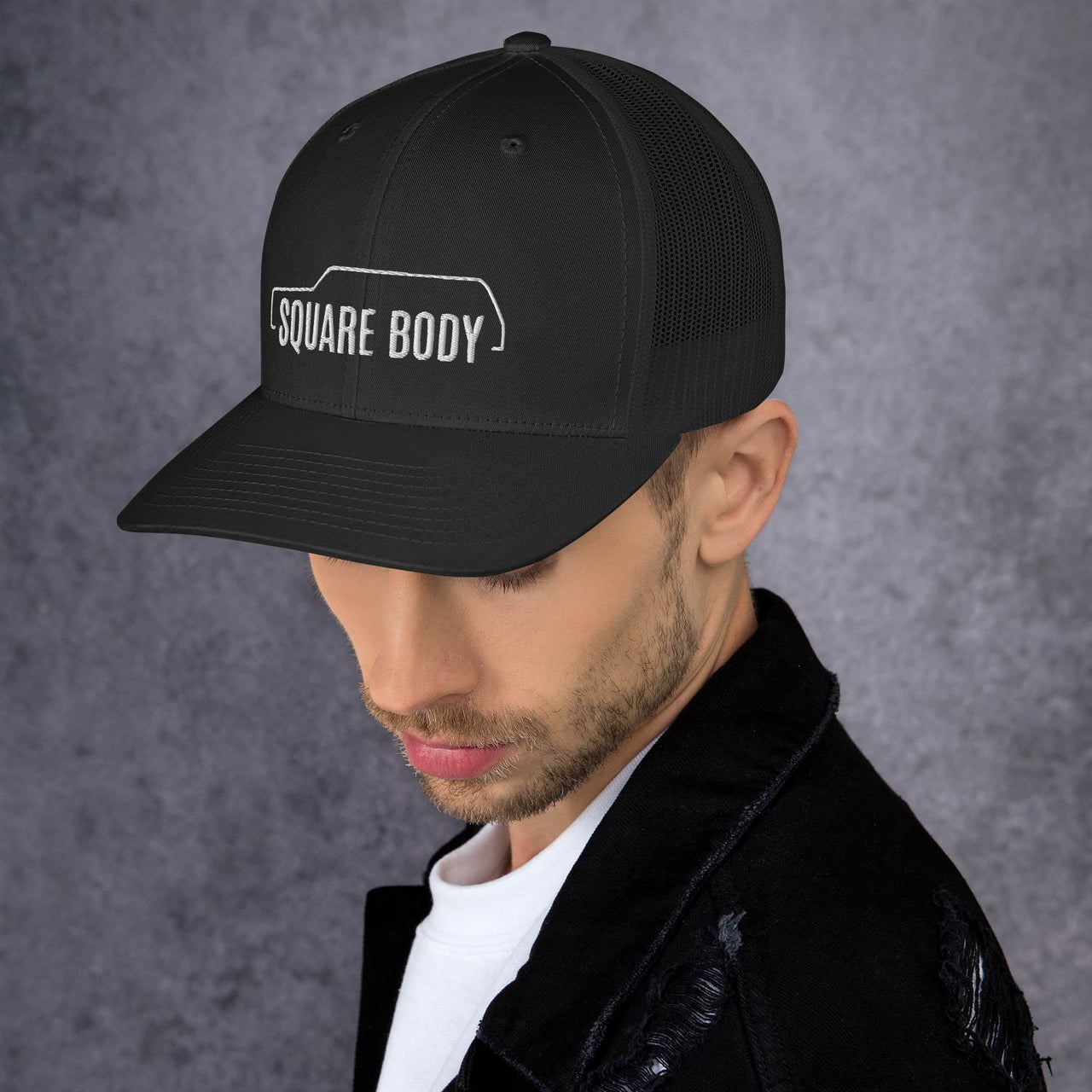 man wearing a 3/4 view of a square body suburban trucker hat from aggressive thread in black
