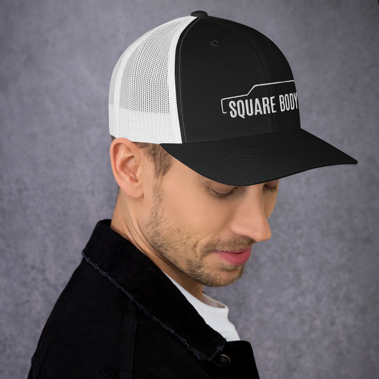 man wearing a 3/4 view of a square body suburban trucker hat from aggressive thread in black and white
