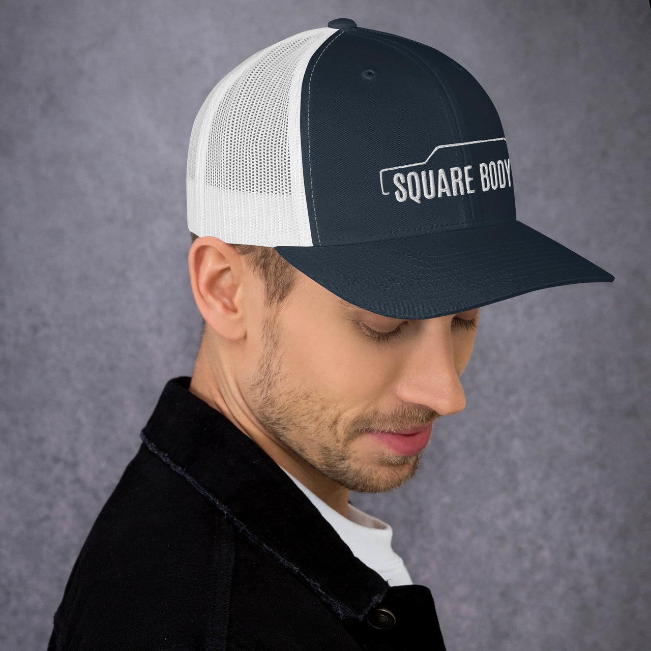 man wearing a 3/4 view of a square body suburban trucker hat from aggressive thread in navy and white